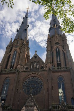Utrecht 'te ikiz kuleleri, bir gül penceresi, sivri kemerleri ve ağaç dalları ve parlak gökyüzü tarafından çerçevelenmiş karmaşık oymaları olan Gotik bir kilisenin cephesi..