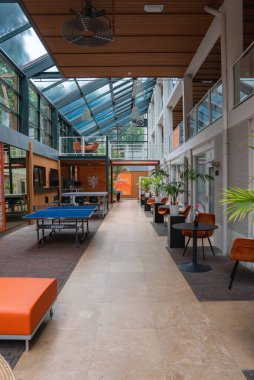 Cam tavanı, masa tenisi masası, turuncu koltuklar, saksı bitkileri ve muhtemelen Utrecht 'te bulunan turuncu amblemli cam duvarları olan kapalı bir alan..