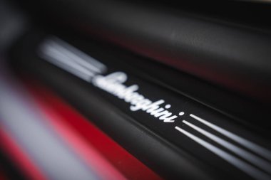 Lamborghini logosunun parlak beyaz çizgileri olan siyah bir yüzeye yakın görüntüsü. Arkaplanda bulanık kırmızı bir element tasarıma karşıtlık ekler.