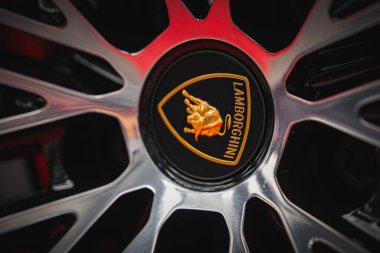 Lamborghini Urus çarkının altın bir boğa amblemi, parlatılmış gümüş teller ve siyah arka planda kırmızı aksanlı bir görüntüsü var..