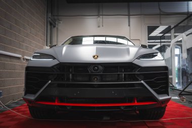 Lamborghini Urus, kırmızı kareli bir zemine park etmiş, keskin LED farlar, kalın bir ızgara ve endüstriyel sergi elementleri ile.