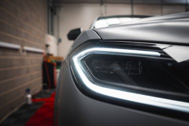 Lamborghini Urus 'un açılı LED tasarımı, mat gri kaplama, tuğla duvarlar ve kırmızı döşeme içeren bir garaj arka planı yakın plan..