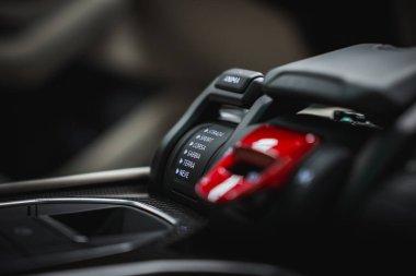 Görüntü Lamborghini Urus 'un merkezi konsolunu yakalar, sürücü modu seçicisi, kırmızı motor başlatma düğmesi ve karbon fiber aksanları içerir..