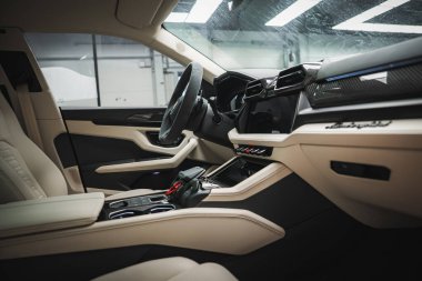 Lamborghini Urus 'un içini yakından görmek bej renkli deri koltuklar, karbon fiber gösterge paneli, modern kontroller ve arka plan gibi bir garaj..