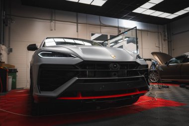 Kırmızı aksanlı Matte Lamborghini Urus, keskin LED farlar, ve iyi aydınlatılmış bir garajda amblem araçlar, ekipmanlar ve kareli döşeme.
