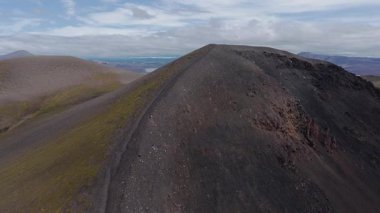 Karanlık arazi, yeşil yosun, dolambaçlı nehir ve bulutlu bir gökyüzünün altındaki uzak dağ sıraları ile İzlanda 'nın volkanik ovasını süpüren hava manzarası..