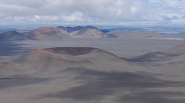 İzlanda 'nın volkanik arazisinin kırmızı renkli bir krateri, engebeli tepeleri, uzak dağları ve arka planda bir nehrin ipucunu gösteren hava manzarası..