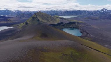 İzlanda 'nın volkanik arazisi üzerinde pürüzsüz bir hava tabakası krater gölü, yeşil yosun kaplı dağ ve uzaktaki karlı zirveleri ortaya çıkarıyor..