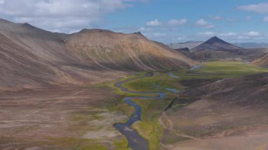 Engebeli tepeleri, sivri bir dağ zirvesi ve İzlanda dağlarında açık mavi gökyüzü olan yeşil bir vadiden geçen dolambaçlı bir nehrin havası..