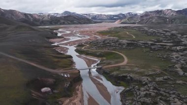 Çok renkli dağları, volkanik arazisi, karla kaplı zirveleri ve küçük bir köprüsü olan engebeli İzlanda Vadisi 'ndeki dolambaçlı bir nehrin havadan tepesi..
