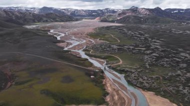 Kıvrımlı bir nehri, küçük bir köprüsü, engebeli dağları, volkanik toprağı ve karlı zirveleri olan İzlanda vadisinin havadan tepesi..