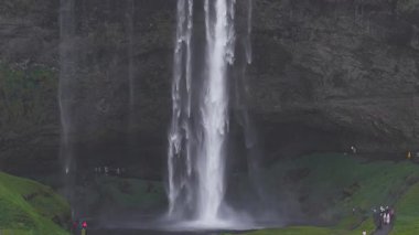 İzlanda 'daki Seljalandsfoss şelalesinin hava manzarası sisli bir uçurumdan dökülen, çimenli tepeler ve engebeli kayalarla çevrili..