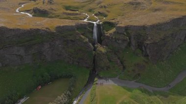 Uçurumlar, otlak düzlükler, dolambaçlı yollar ve İzlanda 'daki uzak dağlarla çevrili bir vadiye akan bir şelalenin havadan görünüşü..