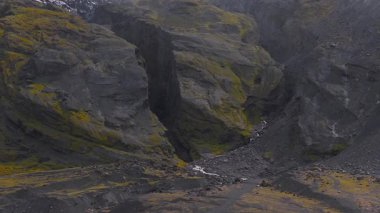 Yeşil yosunlu dik volkanik kayalıklar, kayalık bir vadide akan bir dere ve buzulun yanında kar ve buz farklı bir İzlanda manzarası yaratır..