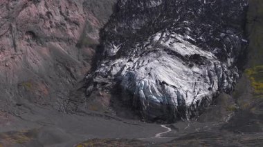 İzlanda 'daki bir buzulun havadan görünüşü, sivri uçlu kenarları, buzlu yarıkları, volkanik araziyi ve yavaş çekim yeşil bitki örtüsünü gösteriyor..