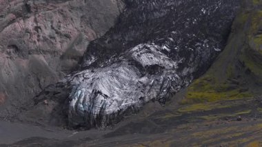 Kül kaplı buzul, sarp kayalıklar ve engebeli İzlanda arazisindeki yeşil yosunları sisli bir atmosfer altında süpüren hava manzarası..