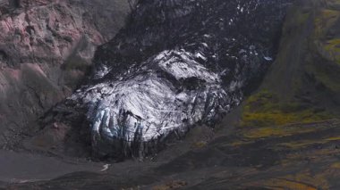 Buzlu yüzeyi, karanlık volkanik arazisi, yosunlu arazisi ve çorak bir vadiden akan dolambaçlı bir deresi olan İzlanda 'daki bir buzulun havadan görünüşü..