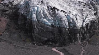 İzlanda 'daki bir buzulun hava görüntüsü, mavi ve beyaz buz oluşumlarını, eriyen nehirleri, kayalık arazileri ve yeşil yosun parçalarını gösteriyor..