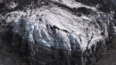 İzlanda 'da koyu buz, beyaz ve mavi çizgiler ve arka planda kırmızımsı kahverengi kayalıklar olan engebeli bir buzulun havadan görünüşü..
