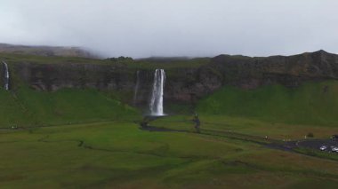 Seljalandsfoss şelaleleri İzlanda 'da yeşil tarlalarla çevrili yüksek bir uçurumdan dökülüyor. Bir yürüyüş yolu ve daha küçük bir şelale de görülebilir..