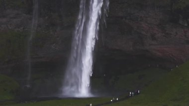 İzlanda 'daki Seljalandsfoss şelalesinin havadan görünüşü, yüksek bir uçurumdan suyla dolu, yemyeşil bir araziyle çevrili, sisli bir spreye dökülen su..