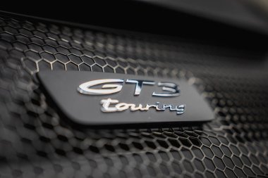 Siyah bir bal peteği ızgarasına monte edilmiş bir Porsche 911 GT3 'ün GT3 tur rozetinin yakın görüntüsü. Metalik harfler ışığı içeri yansıtır..