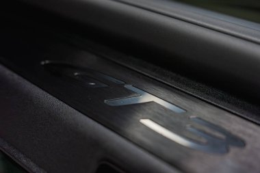 Karanlık bir yüzeyde fırçalanmış metal bir GT3 ambleminin detaylı bir görüntüsü. Kapalı bir garajda özel bir işçilik sergiliyor..