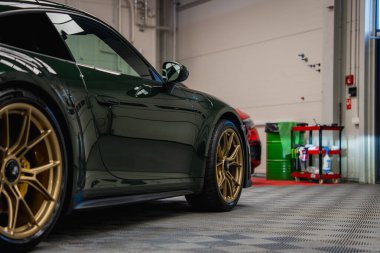 Koyu yeşil bir Porsche 911 GT3. Akort garajında altın tekerlekleri olan bir tur. Aletler, kırmızı bir araba ve yeşil variller arka planda görünür..