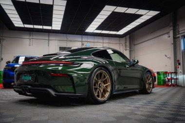 Yeşil bir Porsche 911 GT3 altın tekerlekleri olan bir tur modern bir akort garajında park edilmiş. Tavanı siyah, parlak ışıkları ve görünür aletleri var..