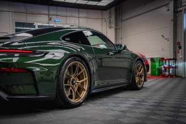 Altın tekerlekleri olan yeşil bir Porsche 911 GT3 iyi aydınlatılmış bir akort garajında park halinde. Tepedeki ışıklandırma parlak tasarımını ve parlak sonunu vurguluyor.