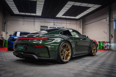 Yeşil bir Porsche 911 GT3 altın tekerleklerle dolu bir tur modern bir akort garajına park edilmiştir. Dişli döşeme, parlak ışıklandırma ve görünür aletleri vardır..