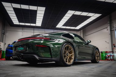 Altın tekerlekli yeşil bir Porsche 911 GT3 modern bir akort garajında park halinde. Parlak tavan ışıkları parlak dizaynını ve çift egzozunu vurgular.