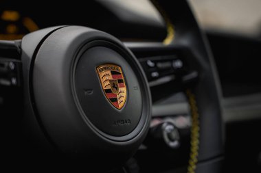Porsche 911 GT3 'ün yakın görüntüsü. Siyah deri ve sarı dikişli direksiyon simidi. Bir akort garajında, bulanık gösterge paneli detaylarıyla birlikte..