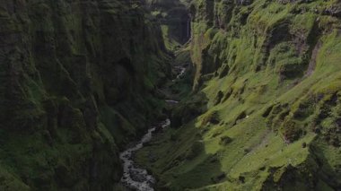 İzlanda 'daki yemyeşil bir kanyonun havadan görünüşü yosun kaplı uçurumlar, çağlayan bir şelale ve kayalık arazide dönen bir dere..