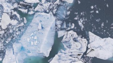 İzlanda 'da beyaz ve mavi buzdağlarının derin mavi sularda sürüklendiği, karmaşık doku ve çatlakları gösteren bir buzul gölünün havadan görünüşü..