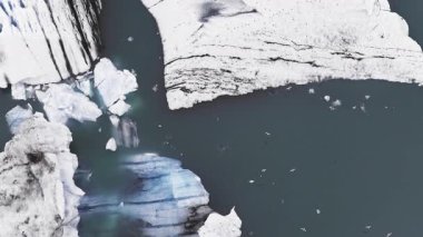 İzlanda 'da devasa buzdağları, volkanik kül siyah çizgileri ve sakin, koyu mavi su üzerinde yumuşak hareket eden bir buzul gölü..