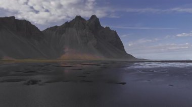 Vestrahorn dağları, siyah kumsal ve kırmızı bir yapıya sahip Stoksnes yarımadasının hava manzarası. Yavaş çekim huzurlu manzarada yankılanır..