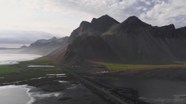 Stoksnes yarımadasındaki Vestrahorn dağlarının hava manzarası, İzlanda. Yavaş hareket siyah kumları, yeşil otları ve kıyı yollarını ortaya çıkarır..