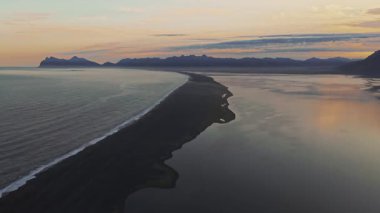 Gün batımında İzlanda 'nın kara kumsal, okyanus ve göl manzarası. Uzakta dağlarla kıyı şeridi boyunca yumuşak bir hareket.