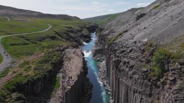 İzlanda 'daki Studlagil Kanyonu' nun havadan görünüşü bazalt sütunlar, turkuaz bir nehir, sarp kayalıklar, yeşillik ve hareket halindeki küçük şelaleler..