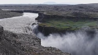 İzlanda 'daki Dettifoss şelalesi güçlü bir şekilde derin bir kanyona dökülür. Sis yükselir ve insanlar engebeli uçurum kenarından izlerler..