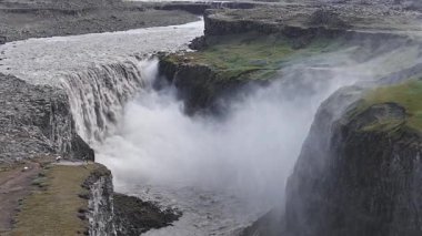 İzlanda 'daki Dettifoss şelalesi, akan su, kayalık arazi, yeşil yamalar ve görülebilir bir izleme platformuyla dolu bir kanyona dalıyor..