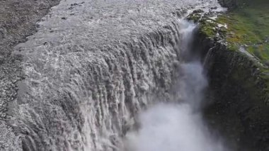 İzlanda 'da Dettifoss şelalesi güçlü bir şekilde kayalık uçurumlara dökülür, sisli sprey, yeşil yosun ve taş adımlı bir patika görünür..