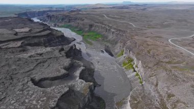 İzlanda 'daki Studlagil Kanyonu' nun havadan görünüşü dik bazalt kayalıkları, kıvrımlı bir nehir, yeşil bitki örtüsü ve kenar boyunca uzanan toprak bir yol gösteriyor..