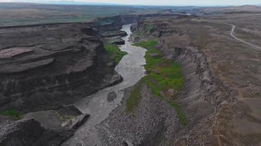 İzlanda 'daki Studlagil Kanyonu' nun havadan görünüşü bazalt sütunlar, kıvrımlı bir nehir, yeşil bitki örtüsü ve arazi boyunca sabit kamera hareketleri sergileniyor..