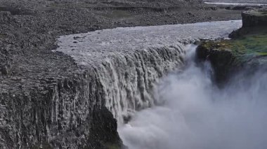 İzlanda 'daki Dettifoss şelalesi, kayalık arazi ve yeşil bitki örtüsüyle çevrili güçlü su hareketiyle sisli bir vadiye daldı..