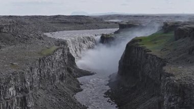 İzlanda 'daki Dettifoss şelalesi, bazalt kaya oluşumları, yeşil yamalar ve mesafeye uzanan bir nehirle çevrili derin bir kanyona daldı..