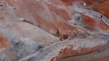 İzlanda 'daki Hver jeotermal alanında kırmızı ve turuncu arazi, yükselen buhar, fümerol, kaynayan çamur havuzları ve ahşap bir yürüyüş yolu bulunur..