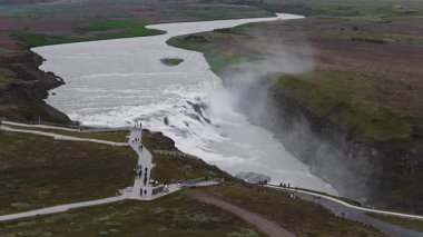İzlanda 'daki Gullfoss şelalesi, dinamik sudan yükselen sisle iki katlı bir kanyona dalıyor. Ziyaretçiler yakınlardaki patikalarda yürürler.