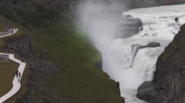 Su Gullfoss şelalesinde güçlü bir şekilde iki kat akar, sis yükselir ve dik uçurumlar İzlanda 'nın dinamik manzarasını sarar..